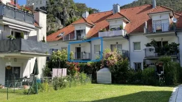 Mehrfamilienhaus mit rotem Ziegeldach, Balkonen und gepflegter Grünfläche im Vordergrund.