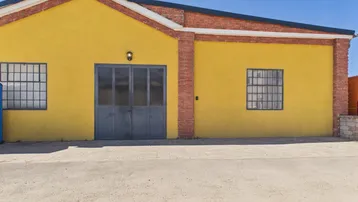 Gelbe Fassade eines Industriegebäudes mit roten Ziegelakzenten, großen Fenstern und einer grauen Doppeltür.
