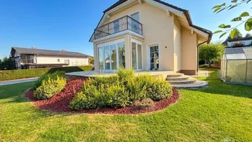 Haus mit Terrasse, Garten und Balkon unter blauem Himmel.
