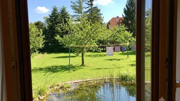 Blick aus dem Fenster auf einen grünen Garten mit Teich und Wäscheleine.