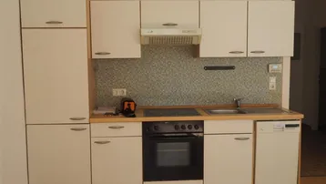 Funktionale Einbauküche mit weißen Schränken, integrierten Geräten und gefliestem Spritzschutz.