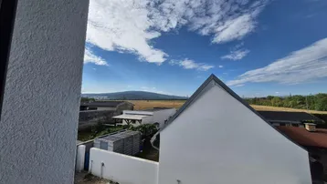 Weitblick über die Landschaft mit Feldern und fernen Hügeln unter blauem Himmel.
