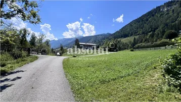 Landstraße führt durch grüne Wiesen mit Blick auf bewaldete Berge und ein entferntes Gebäude.