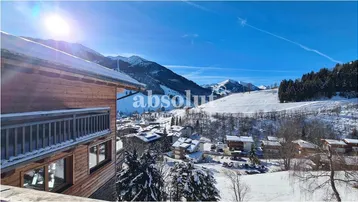 Winterliche Berglandschaft mit schneebedeckten Dächern und einem traditionellen Holzgebäude im Vordergrund.