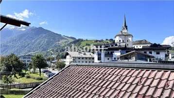 Panoramablick über ein malerisches Dorf mit Kirche und schneebedeckten Bergen im sonnigen Hintergrund.