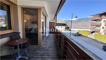 Langer Balkon mit Holzboden, Sitzgelegenheiten und Panoramablick auf die Bergwelt und die Umgebung.