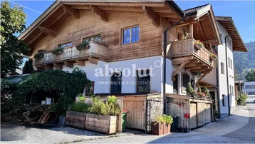 Traditionelles Holzhaus mit weißer Fassade und Balkonen in alpiner Umgebung.