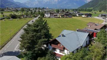 Weitläufige Luftaufnahme der ländlichen Umgebung mit Häusern, Feldern und majestätischen Bergen im Hintergrund.