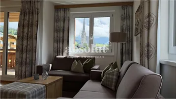 Gemütliches Wohnzimmer mit Sofa, Fensterblick auf die Kirche und alpiner Dekoration.