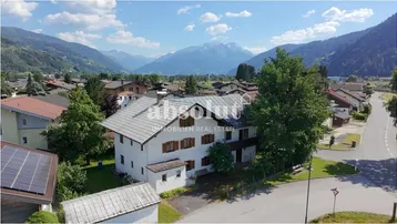 Luftaufnahme eines traditionellen Hauses in alpiner Umgebung mit Bergblick und umliegender Bebauung.