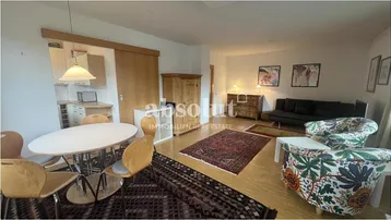 Gemütlicher Wohn-Essbereich mit Holzboden, Teppichen und einem Schrank aus hellem Holz, der den Raum strukturiert.