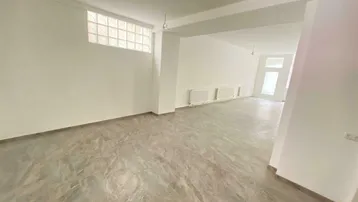 Geräumiger, leerer Gewerberaum mit hellen Wänden, Fliesenboden und einem Glasbausteinfenster.