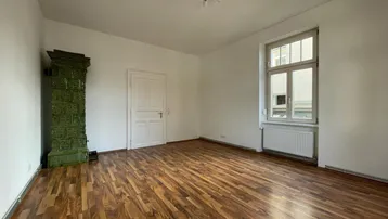 Geräumiges Wohnzimmer mit Holzboden und einem traditionellen grünen Kachelofen.