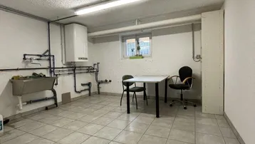 Funktionaler Kellerraum mit Fliesenboden, Waschbecken und sichtbaren Rohren, ideal als Hauswirtschaftsraum.