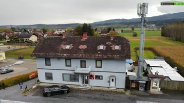 Luftaufnahme des Gebäudes mit umliegender Landschaft, einem Mobilfunkmast und Parkplätzen.