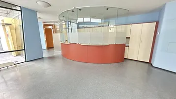 Geräumiger Empfangsbereich mit geschwungener Theke, Glaswänden und hellblauen Akzentwänden, ausgestattet mit Vinylboden.