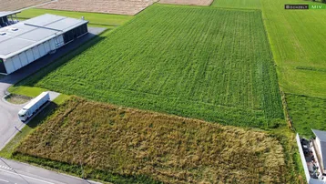 Luftaufnahme von landwirtschaftlichen Feldern, einem Gewerbegebäude und einer Straße mit LKW.