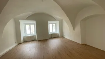 Geräumiger Raum mit einzigartiger Gewölbedecke, Holzboden und zwei Fenstern, die viel Licht hereinlassen.