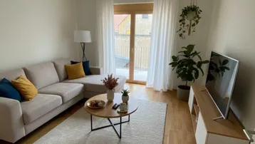Helles Wohnzimmer mit modernem Sofa, Holzboden und Zugang zu einem Außenbereich.
