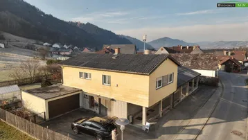 Luftaufnahme eines Einfamilienhauses mit angrenzender Garage und Blick auf die umliegende Berglandschaft.