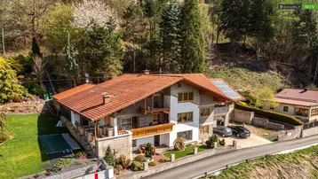 Großzügiges Einfamilienhaus mit rotem Ziegeldach, Solaranlage und gepflegtem Garten in Hanglage.