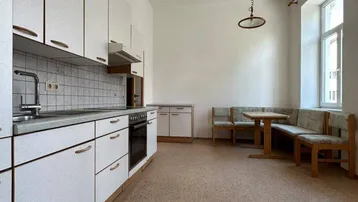 Helle Küche mit weißen Schränken, Fliesenrückwand und integriertem Essbereich am Fenster.