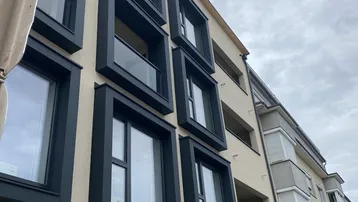 Moderne Gebäudefassade mit markanten schwarzen Fensterrahmen und Balkonen, die einen urbanen Eindruck vermitteln.