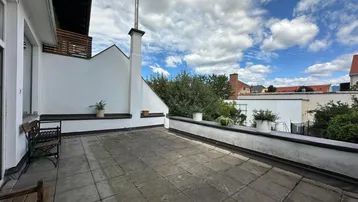 Große gepflasterte Terrasse mit Sitzgelegenheiten und Blick auf den Himmel und umliegende Gebäude.