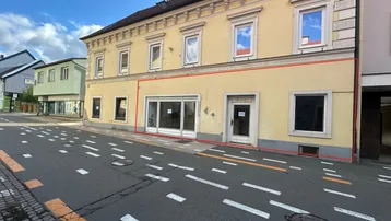 Historisches Gebäude mit gelber Fassade und großen Schaufenstern im Erdgeschoss, direkt an der Straße gelegen.