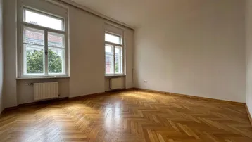Helles Zimmer mit Fischgrätparkett und zwei großen Fenstern, ideal als Wohn- oder Schlafzimmer.