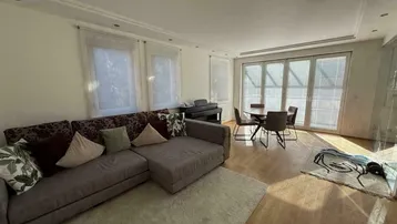 Geräumiges Wohn-Esszimmer mit bequemer Couch, Esstisch und Zugang zu großen Fenstern.
