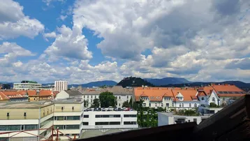 Panoramablick über die Stadt mit Bergen im Hintergrund unter einem weiten, blauen Himmel.