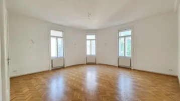 Helles, leeres Zimmer mit Fischgrätparkett und drei hohen Fenstern, bereit zur individuellen Gestaltung.