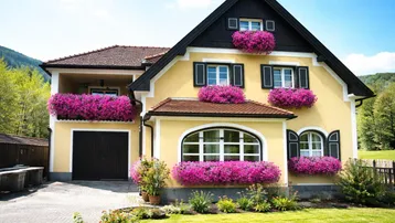 Traditionelles Haus mit gelber Fassade, schwarzen Fensterläden und blühenden Blumenkästen.