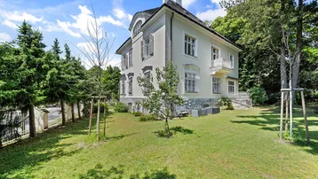 Elegante Villa mit gepflegtem Garten und klassischer Architektur unter blauem Himmel.