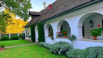 Traditionelles Landhaus mit weißer Fassade, grüner Rasenfläche und überdachtem Bogengang.