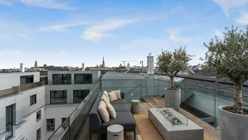 Moderne Dachterrasse mit bequemen Loungemöbeln, Feuerstelle und Blick über die Stadt.