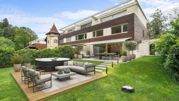 Großer Garten mit Holzterrasse, Whirlpool und gemütlicher Lounge-Ecke vor dem modernen Gebäude.