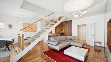 Modernes Wohnzimmer mit offener Treppe, bequemer Couch und Holzboden, verbunden mit dem Küchenbereich.