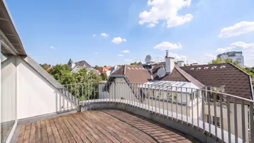 Geräumige Dachterrasse mit Holzboden und Blick über die Dächer der Stadt unter blauem Himmel.