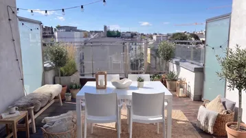 Helle Dachterrasse mit Esstisch, Sitzbank und Lichterkette, ideal für entspannte Stunden im Freien.