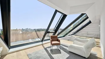 Helles Wohnzimmer mit großen, schrägen Fenstern, die einen weiten Stadtblick bieten.
