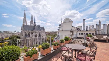 Große Dachterrasse mit schmiedeeisernen Möbeln und beeindruckendem Blick auf eine historische Kirche.