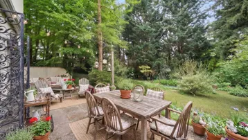 Große Terrasse mit Essbereich und Lounge-Möbeln, umgeben von üppigem Grün und Bäumen.