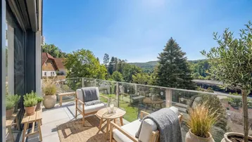 Heller Balkon mit Glasgeländer, bequemen Gartenmöbeln und weitem Blick ins Grüne.