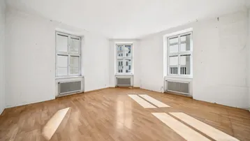Helles Zimmer mit Parkettboden und drei Fenstern, das viel Tageslicht hereinlässt.
