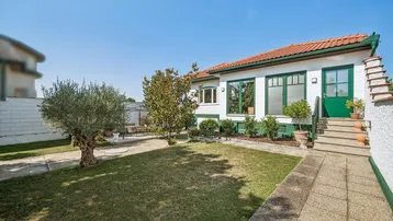 Weißes Einfamilienhaus mit grünen Fensterrahmen, rotem Ziegeldach und gepflegtem Vorgarten.