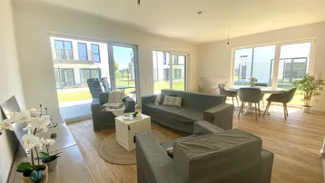 Helles Wohn- und Esszimmer mit Holzboden, großen Fenstern und Zugang zur Terrasse.