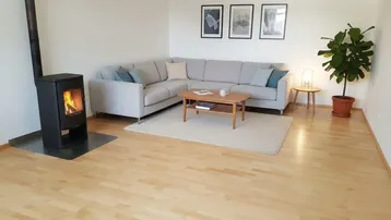Helles Wohnzimmer mit modernem Ecksofa, Holzboden und gemütlichem Kaminofen.