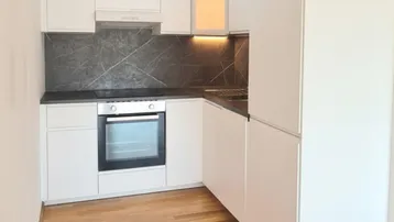 Moderne Einbauküche mit weißen Hochglanzfronten, dunkler Arbeitsplatte und Holzfußboden.